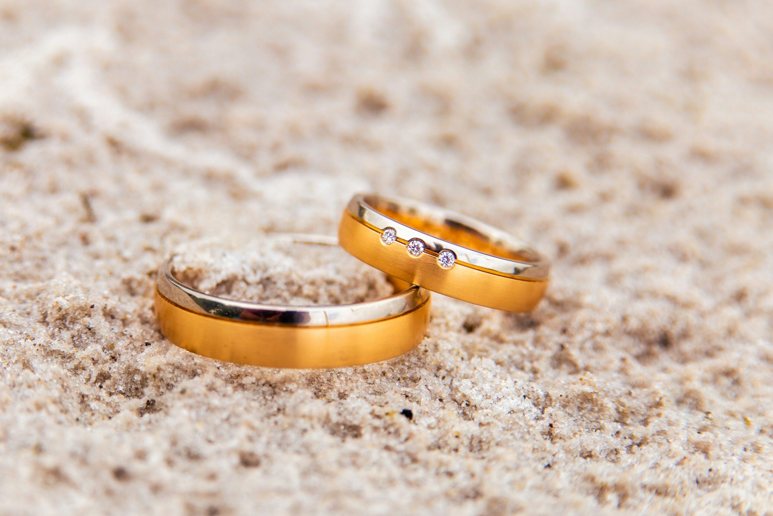 Dos argollas de matrimonio doradas sobre arena.