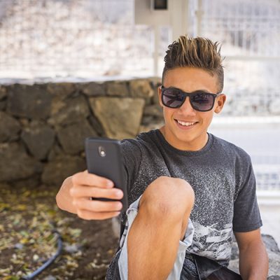 Young handsome teenager boy 15 years old take selfie picture with mobile phone smiling to the device - social media life for influencer and blogger - new work with internet
