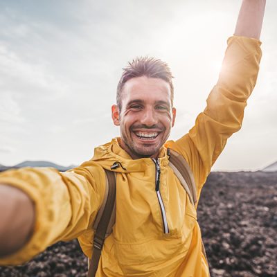 Handsome man taking a selfie climbing a rock. Smiling hiker taking a portrait with action cam hiking a mountain at sunset.
